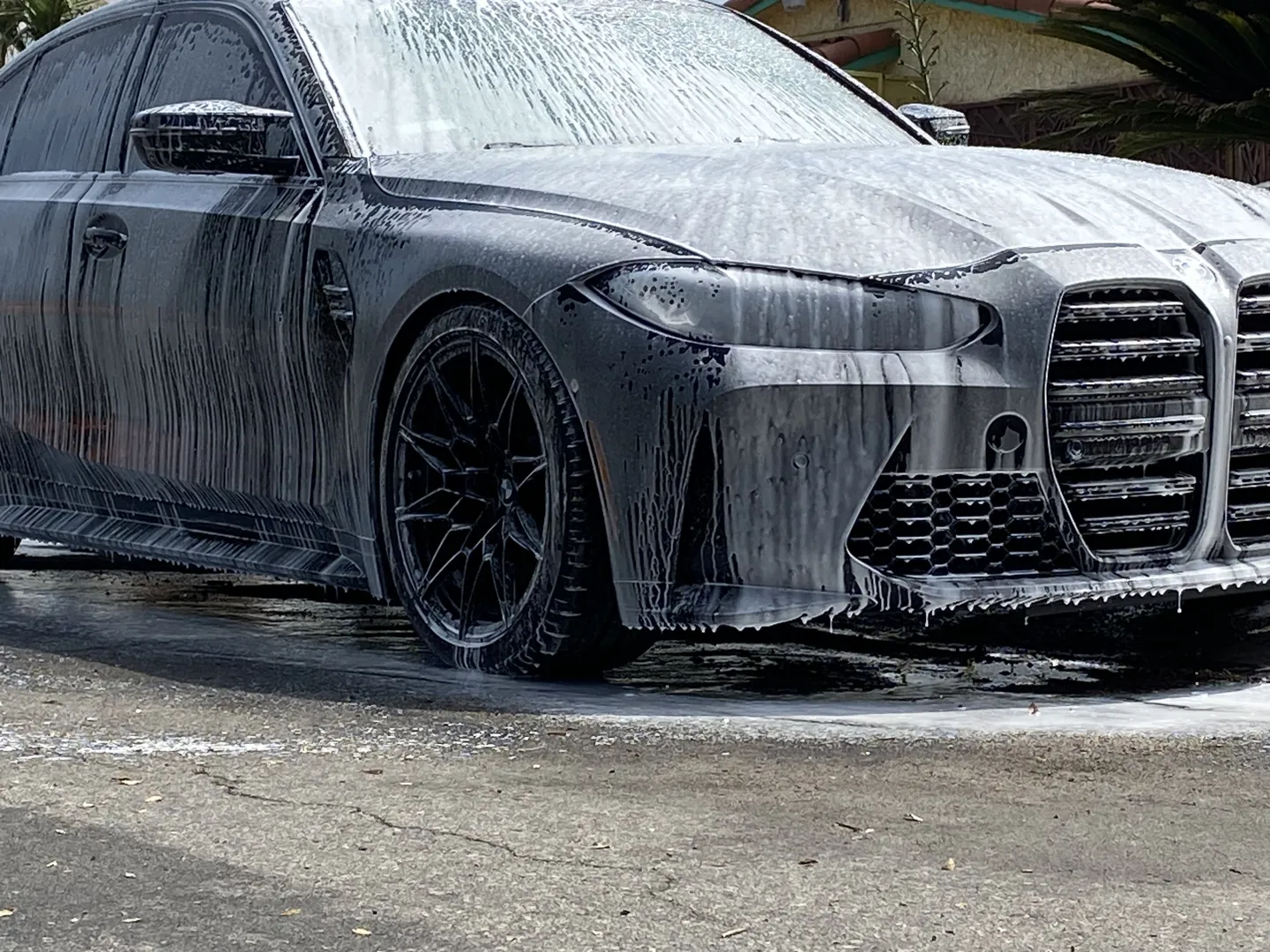 Black BMW covered in thick wash foam during an exterior wash